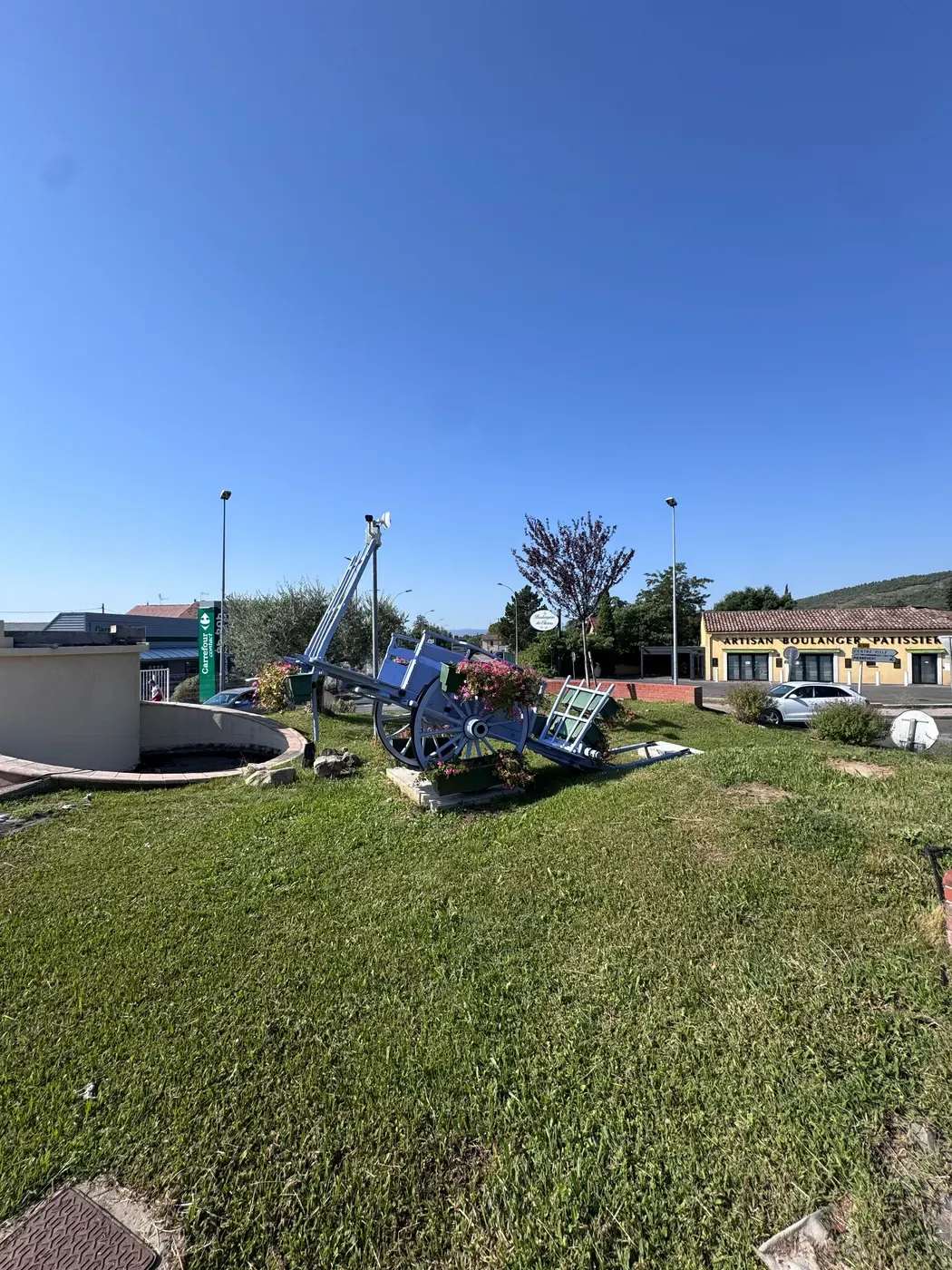 Une charrette provençale peinte en bleu et garnie de fleurs, posée sur un rond-point du centre de Sainte-Tulle.