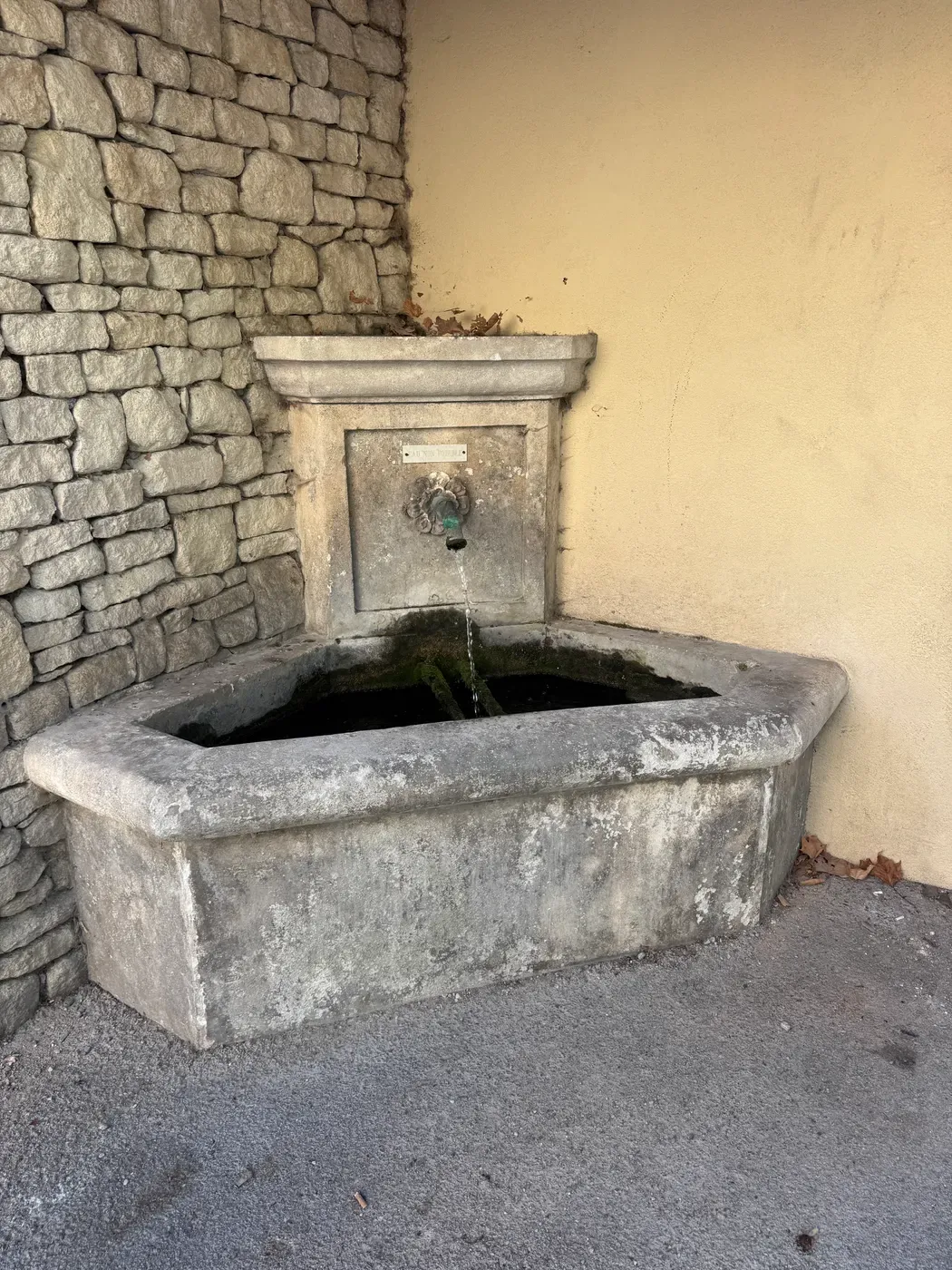 Une fontaine ancienne en pierre adossée à un mur, l’eau coulant dans son bassin, à Volx.